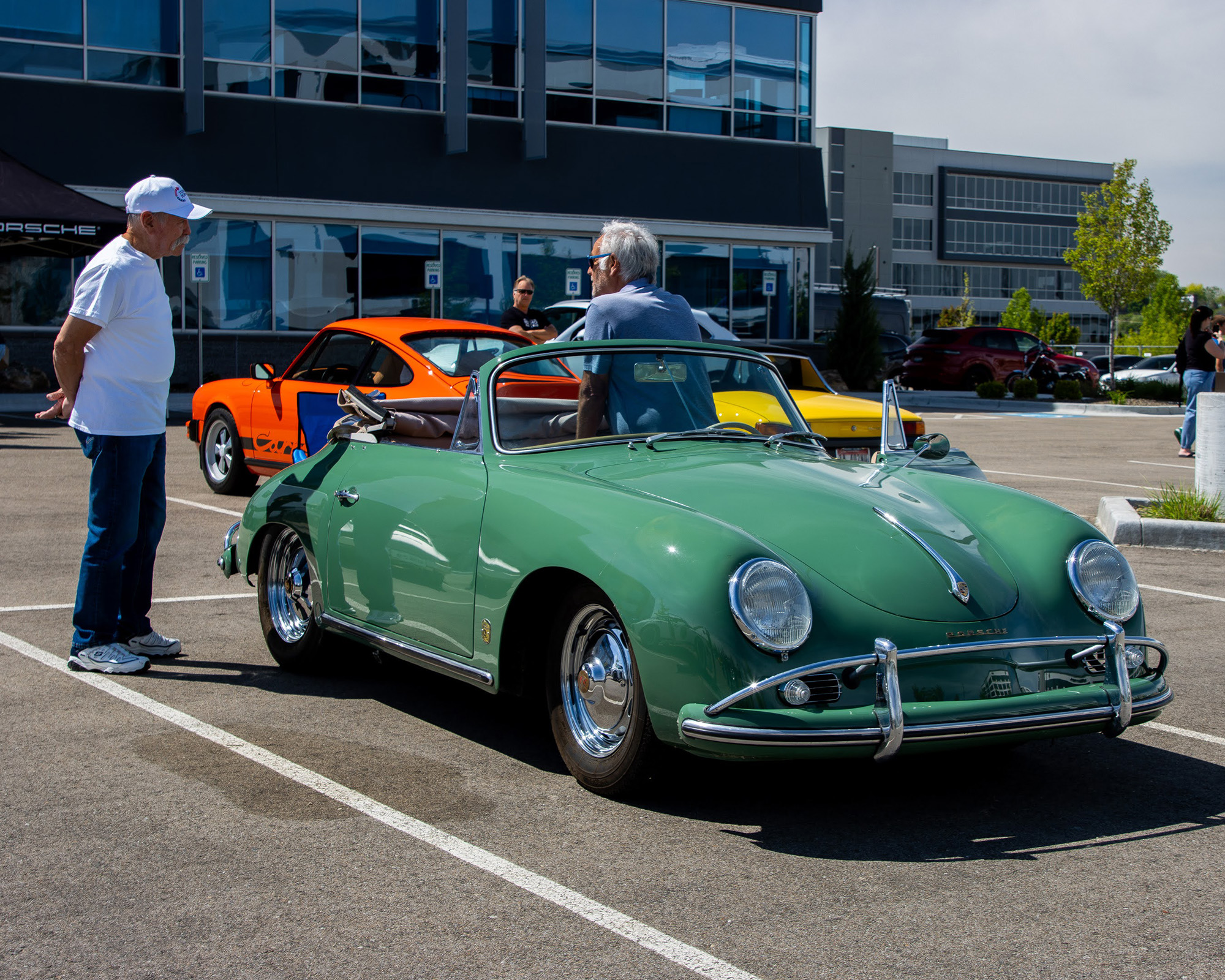A green Porsche 356 cabriolet parked in the lot with two men talking beside it