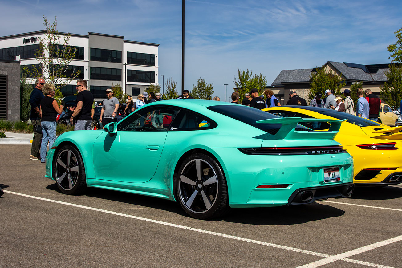 Mint green Porsche 911 with an aero kit rear wing at Idaho Air 2026, parked beside a yellow 911 with the crowd behind