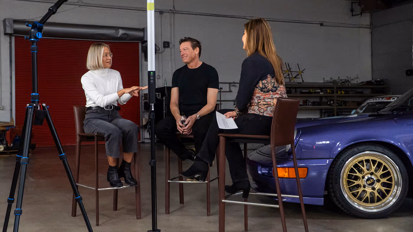 Kelly and Daria Smith being interviewed in a garage beside a purple Porsche